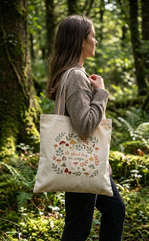 Person carrying the Glasóg Ar shiúl leis na sióga tote bag in an Irish woodland, recycled cotton with rainbow webbing handles.