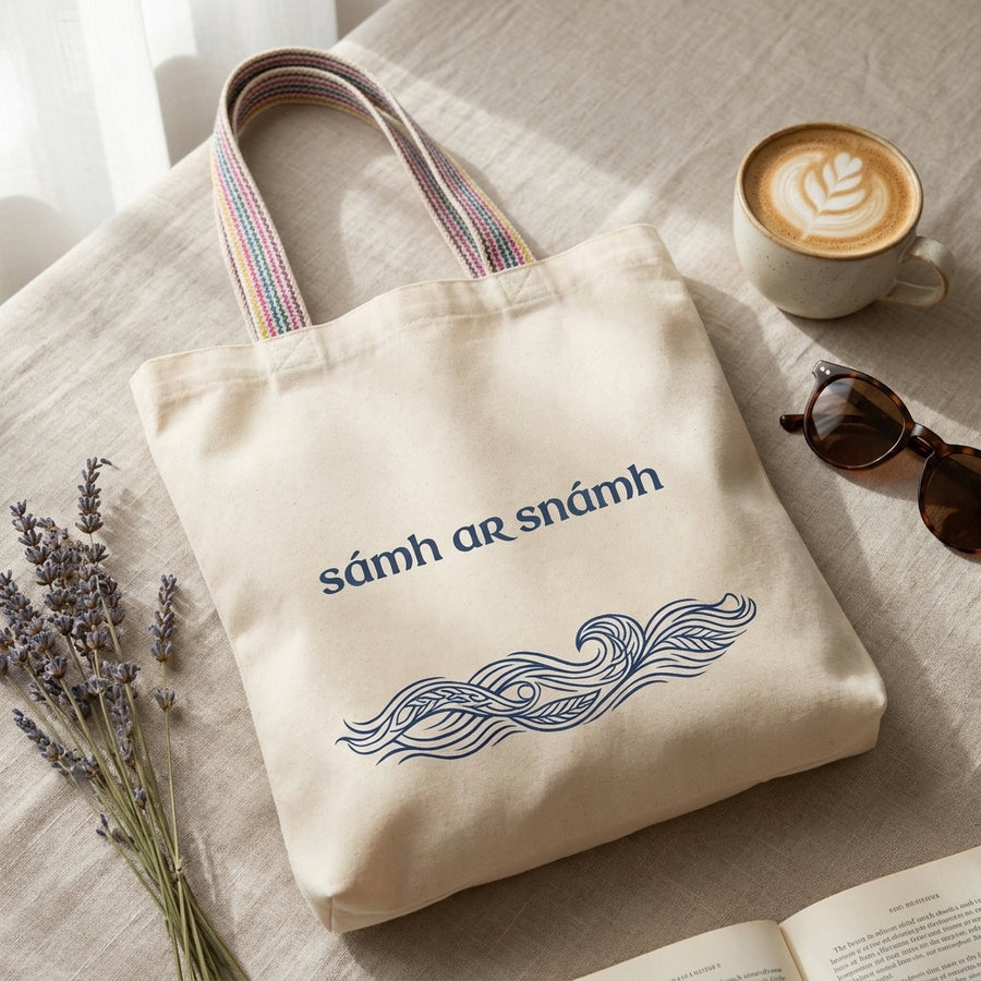 Flat lay of a Sámh ar Snámh tote bag with coffee and lavender — Glasóg Irish language recycled cotton shopper with Gaeilge wave design.