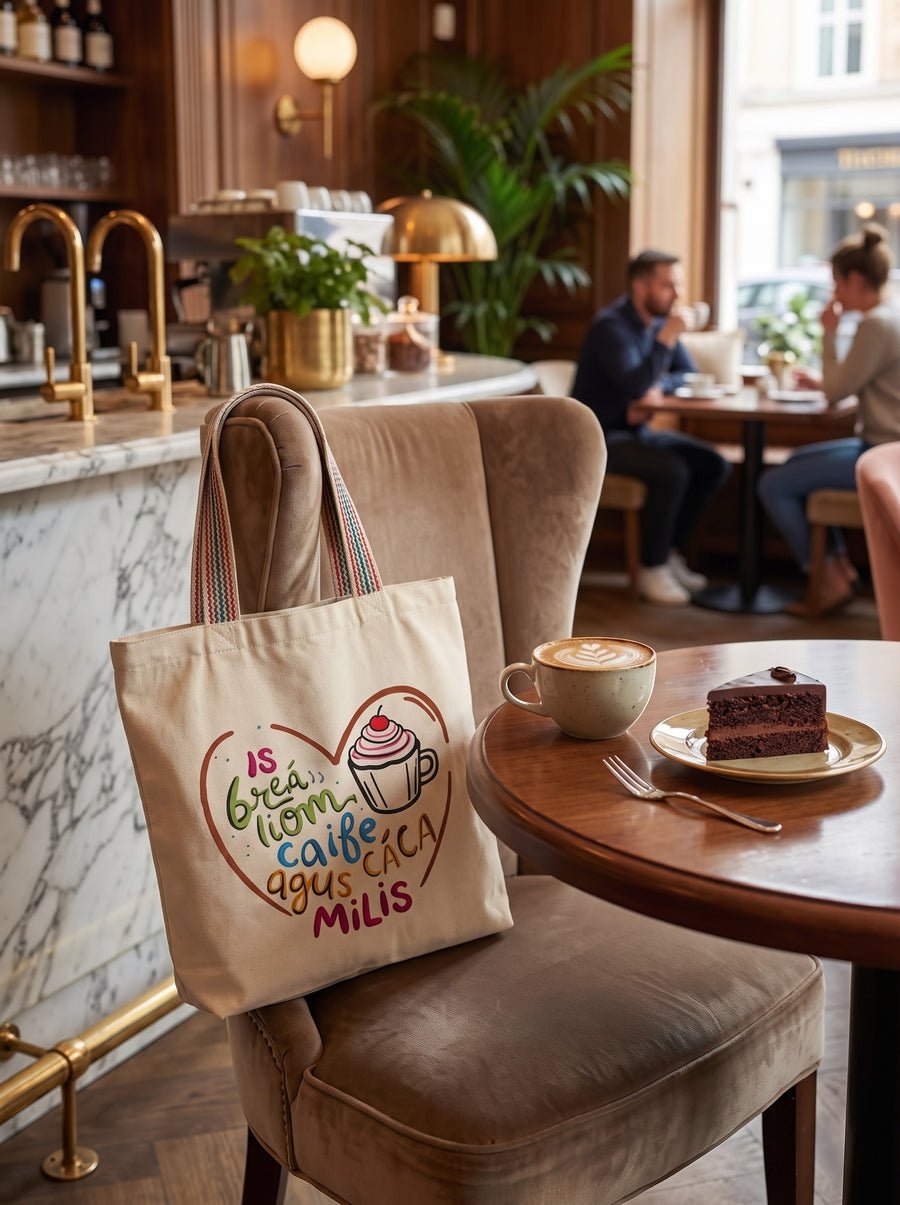 Is Breá Liom Caife agus Cáca Milis tote bag on a café chair with coffee and cake