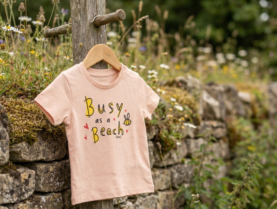 peach Baby Creator t-shirt with bee design — on a hanger outdoors