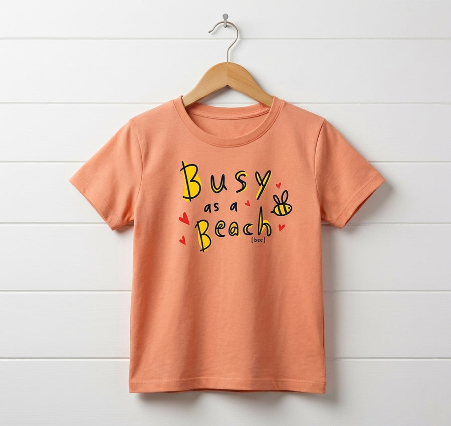 peach kids t-shirt with bee design hanging on wooden shiplap wall