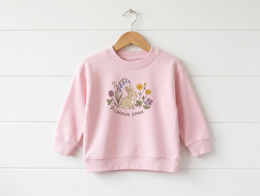 pink kids sweatshirt with rabbit-floral design hanging on wooden shiplap wall