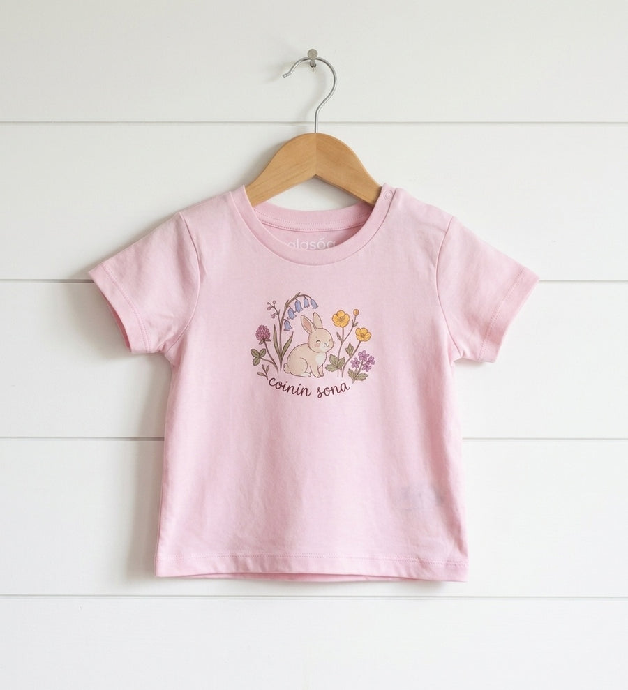 pink kids t-shirt with rabbit-floral design hanging on wooden shiplap wall