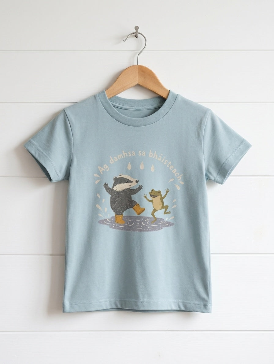 seafoam kids t-shirt with badger-frog design hanging on wooden shiplap wall