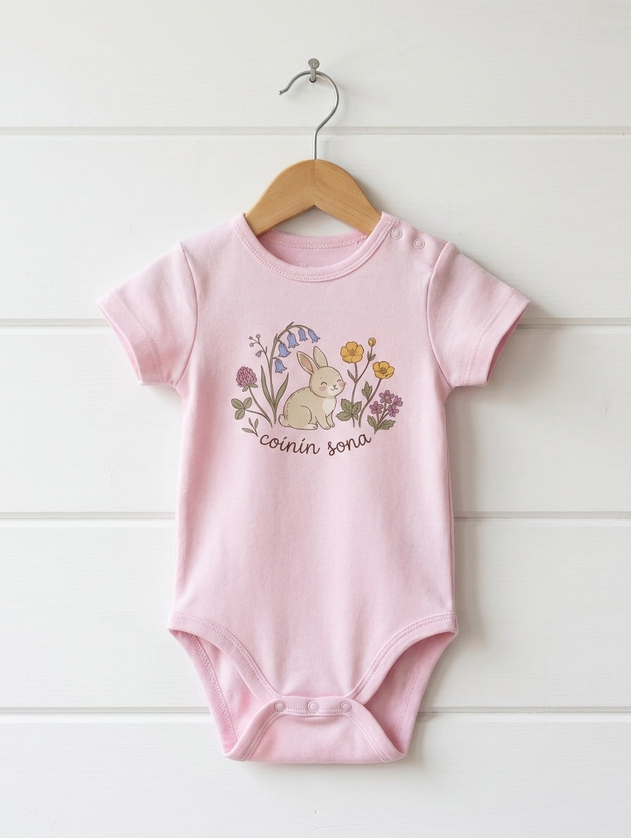 pink kids bodysuit with rabbit-floral design hanging on wooden shiplap wall