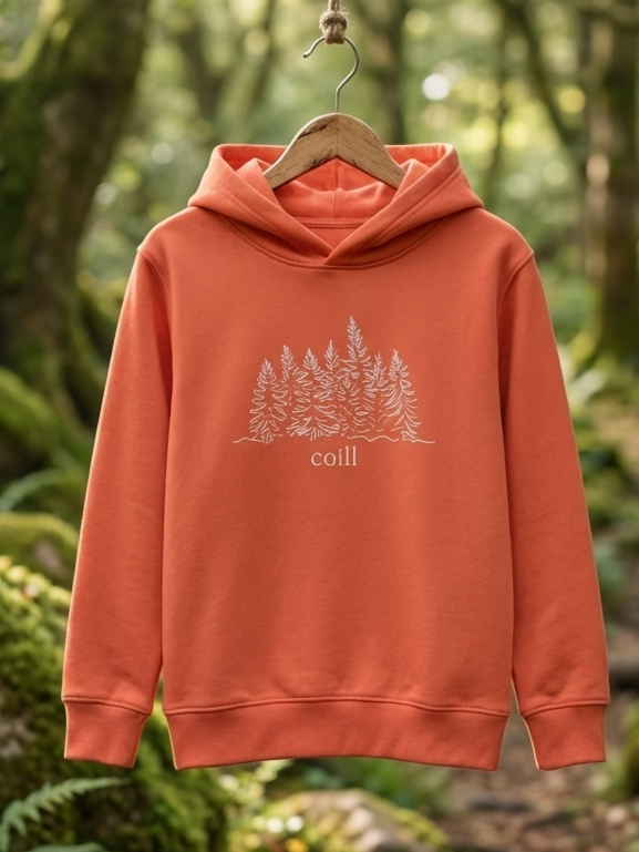 Orange Coill kids hoodie hanging on a wooden hanger in an Irish forest