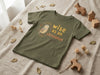 Flat lay of olive t-shirt with owl design on natural leaf background