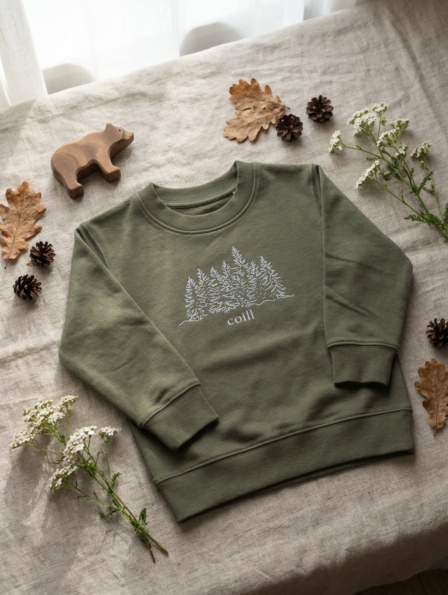 Flat lay of olive sweatshirt with trees design on natural leaf background
