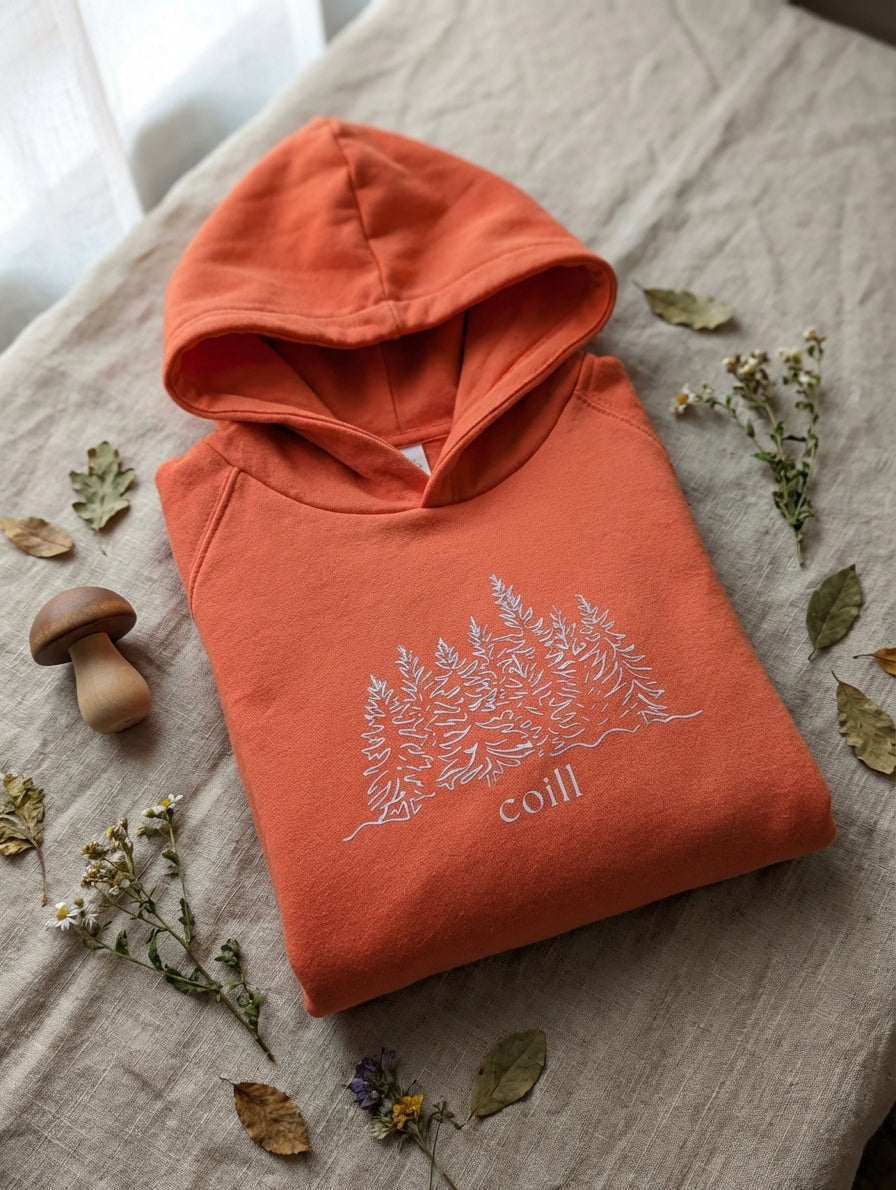 Flat lay of orange hoodie with trees design on natural leaf background