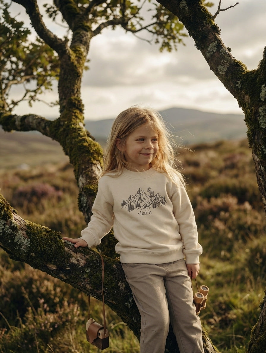 Styled editorial photo of beige kids sweatshirt with mountain illustration
