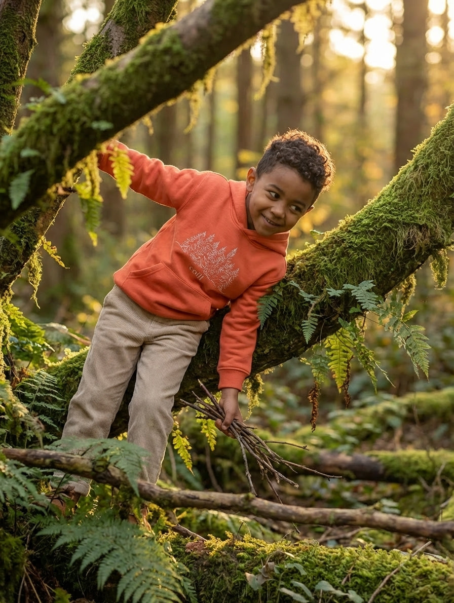 Styled editorial photo of orange kids hoodie with trees illustration