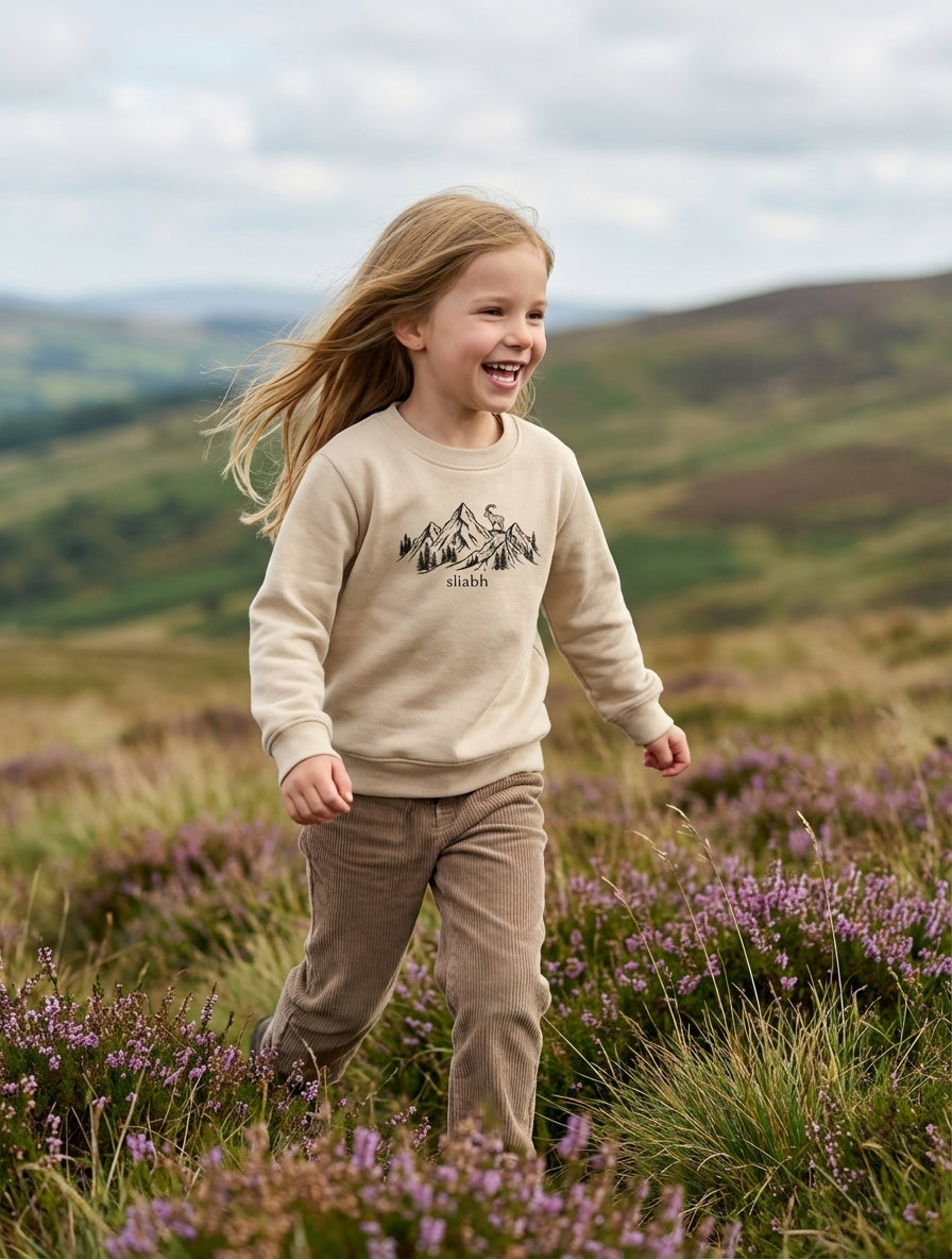 Child in motion wearing beige sweatshirt with mountain design