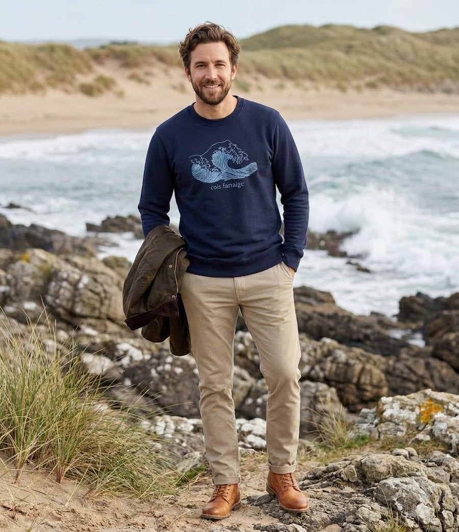 Man wearing the navy Cois Farraige adult sweatshirt on a rocky Atlantic beach