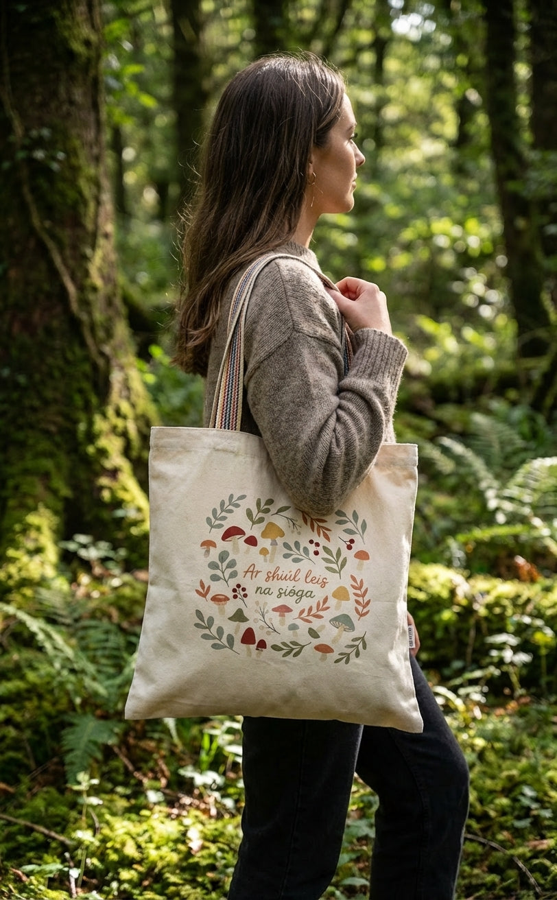 Person carrying the Glasóg Ar shiúl leis na sióga tote bag in an Irish woodland, recycled cotton with rainbow webbing handles.