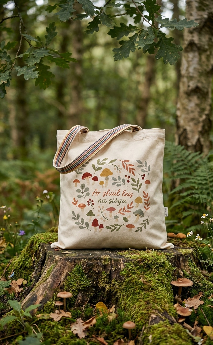 Glasóg Ar shiúl leis na sióga tote bag resting on a mossy tree stump in an Irish forest, surrounded by ferns.